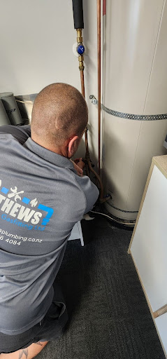 Plumber working on copper pipework beside a hot water cylinder during installation or servicing inside a home.